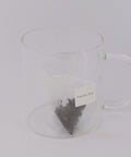 Preparación de té Oolong Melocotón en bolsita piramidal, infusionándose en agua caliente y liberando notas afrutadas.