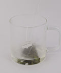Preparación de té Dragon Well en bolsita piramidal, infusionándose en agua caliente mientras las hojas se expanden y liberan su aroma.